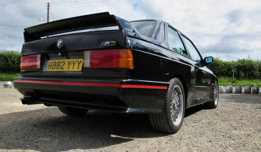 BMW M3 E30 noire vue arrière droite avec grand aileron