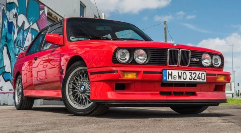 BMW M3 E30 rouge vue de face trois quarts avec badge M3 visible et jantes BBS sur route