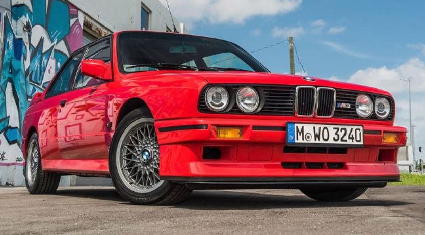 BMW M3 E30 rouge vue de face trois quarts avec badge M3 visible et jantes BBS sur route