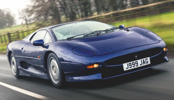 Jaguar XJ220 bleue en mouvement sur route de campagne, vue avant trois-quarts