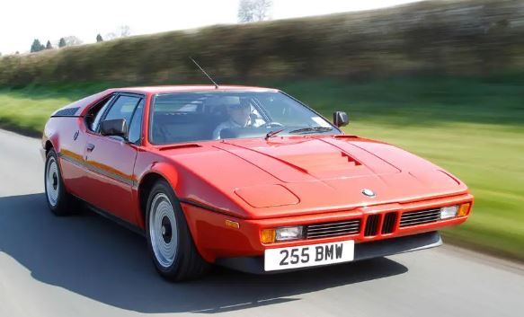 BMW M1 rouge en mouvement vue de face trois quarts sur route avec design de supercar des années 70