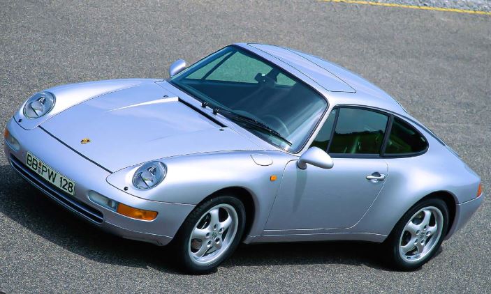 Porsche 911 type 993 gris clair vue de trois quarts avant sur une route dégagée