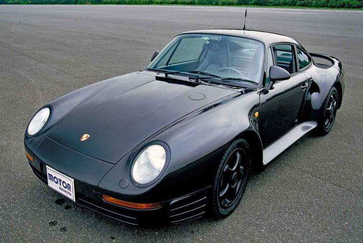 Porsche 959 noire photographiée de trois quarts avant sur une piste d’essai, supercar allemande emblématique des années 1980