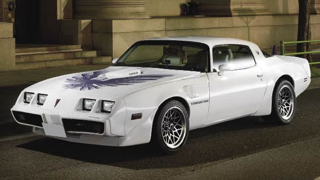 Pontiac Trans Am blanche stationnée de nuit, capot orné du célèbre Screaming Chicken