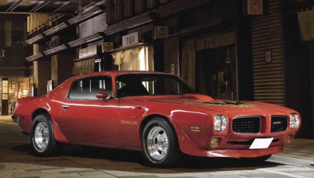 Pontiac Trans Am rouge stationnée dans une rue urbaine de nuit, ambiance ville asiatique