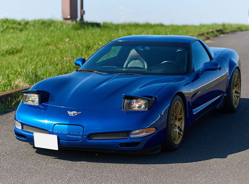 Chevrolet Corvette C5 bleue avec phares escamotables ouverts et jantes dorées, vue de trois quarts avant.