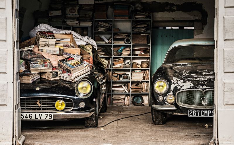 Ferrari et Maserati anciennes oubliées dans un garage rempli d’objets sortie de grange