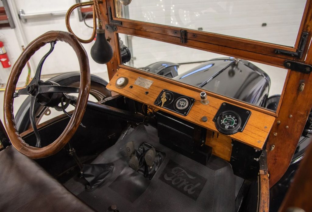 Intérieur de la Ford Model T avec volant en bois, tableau de bord en bois, instrumentation d'époque et trois pédales de commande.