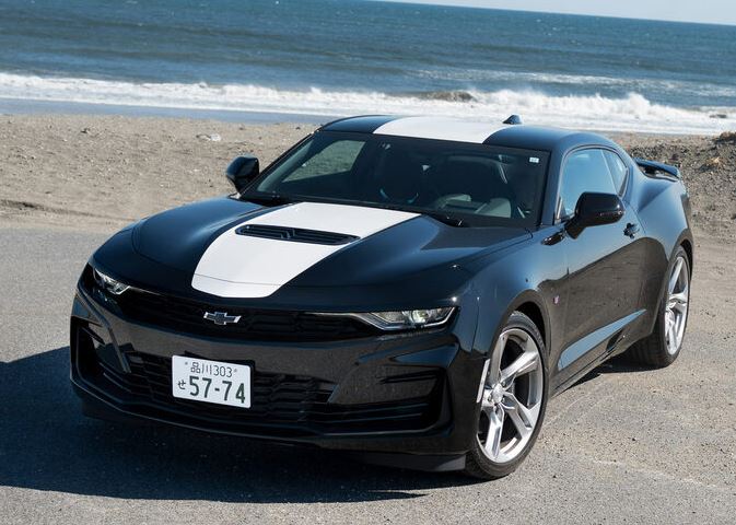 Chevrolet Camaro sixième génération noire à bandes blanches, photographiée de trois quarts avant au bord de la mer.