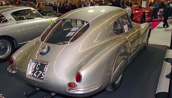 Vue arrière trois quarts d’une Fiat 8V gris clair exposée dans un salon automobile, carrosserie fluide et compacte