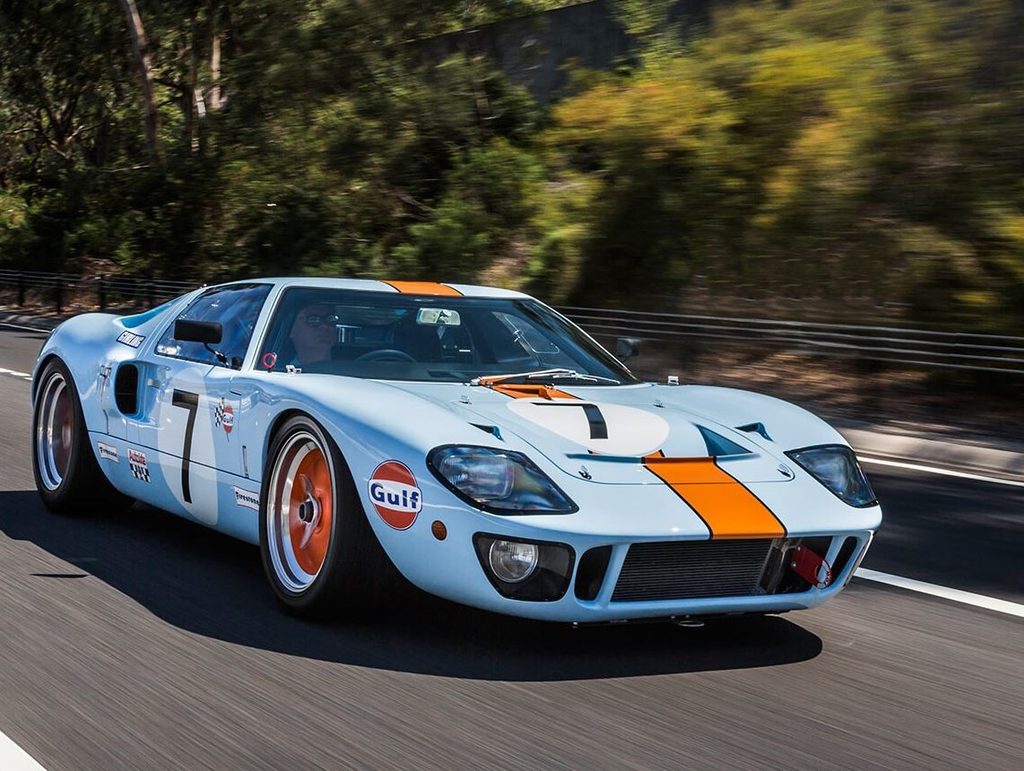 Réplique de Ford GT40 Mk I aux couleurs Gulf bleu et orange, photographiée en mouvement sur route.
