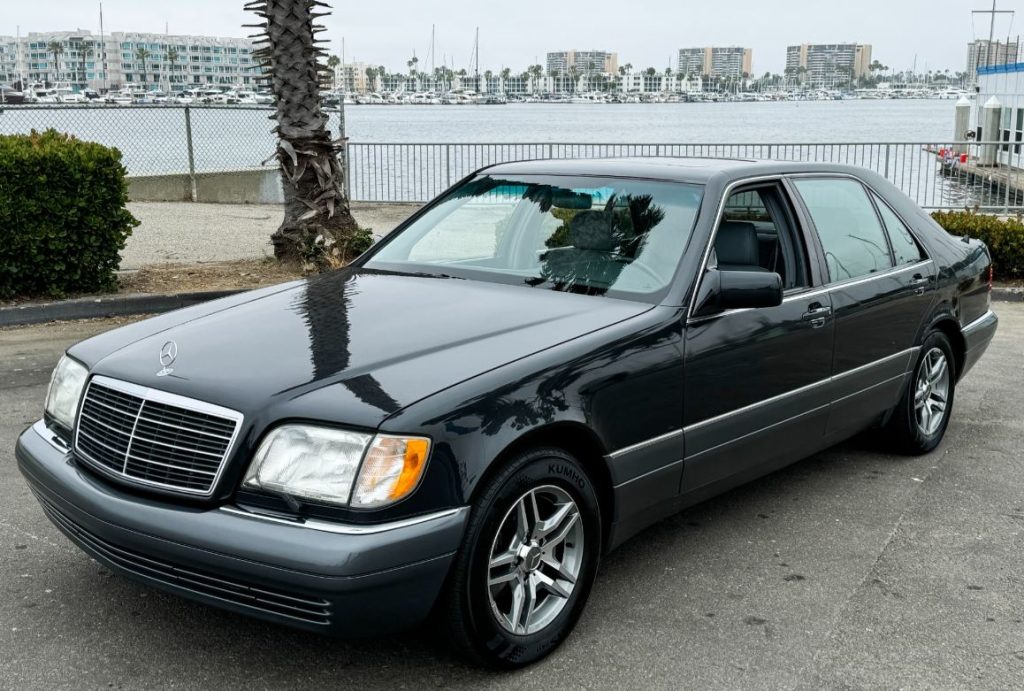 Mercedes Classe S noire des années 90 stationnée près d’un port de plaisance