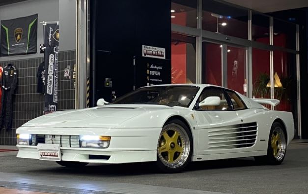 Ferrari Testarossa blanche exposée de nuit devant une vitrine automobile