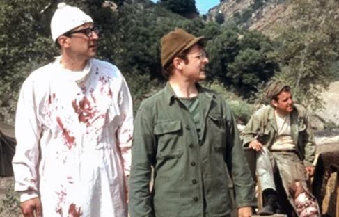 Personnages du film M.A.S.H en tenue militaire devant une Jeep du camp