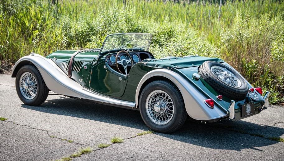 Morgan Plus 4 bicolore stationnée de profil avec capote repliée et roues à rayons