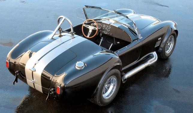 AC Cobra noire à bandes blanches, vue arrière trois-quarts sur sol mouillé