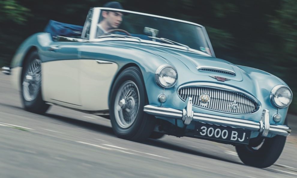 Austin-Healey 3000 cabriolet bleu roulant sur route boisée