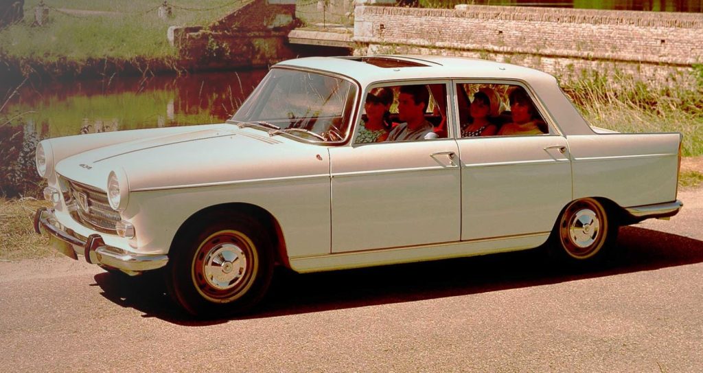 Peugeot 404 blanche roulant avec une famille à bord dans les années 60