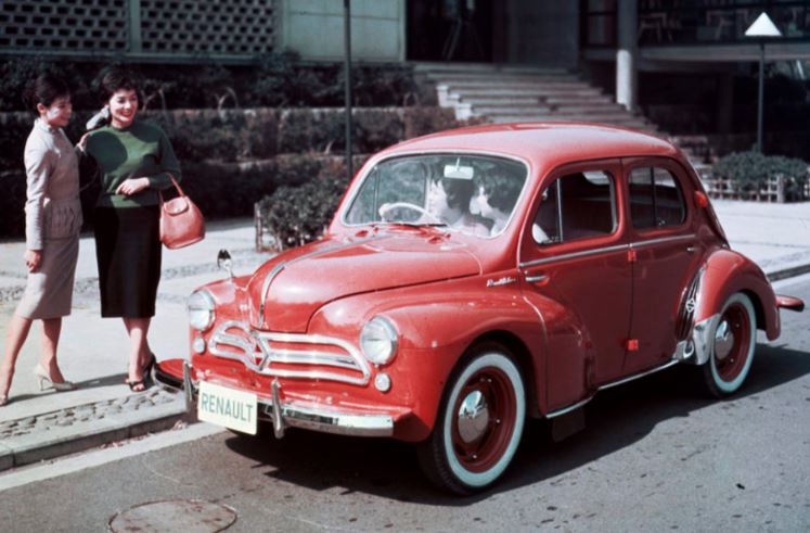 Renault 4CV rouge stationnée en ville avec des passants autour