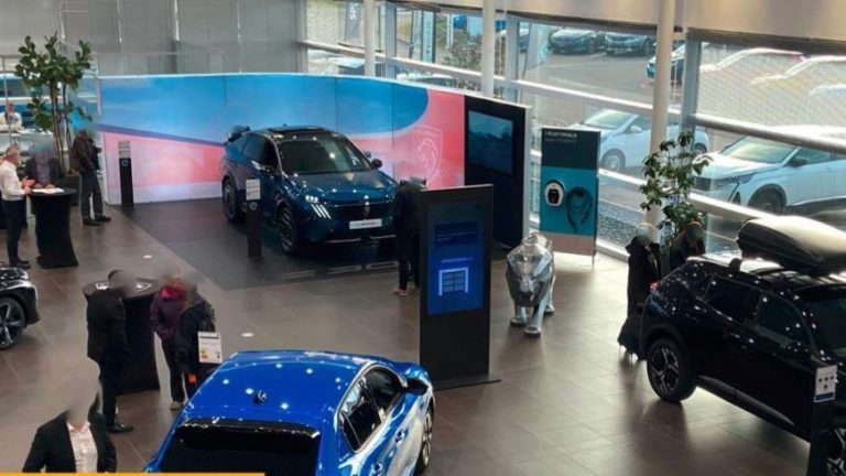 Intérieur de concession automobile avec voitures neuves exposées et clients en discussion