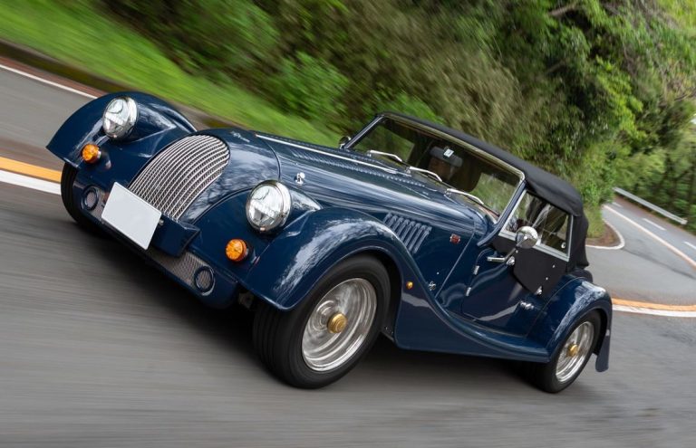 Morgan Plus 4 bleue vue trois quarts avant en roulage sur route sinueuse