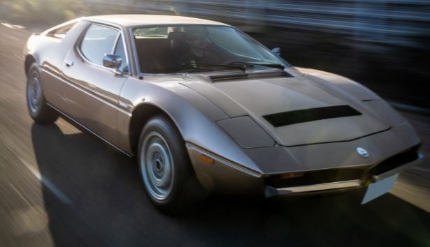 Maserati Merak grise en mouvement sur route, profil avant légèrement flou
