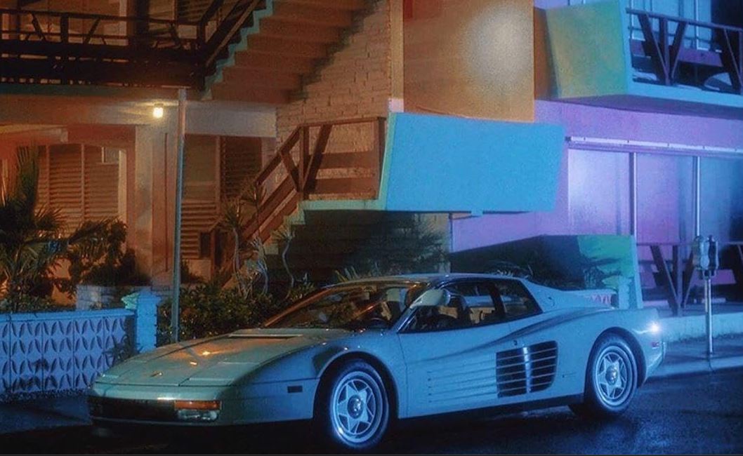 Ferrari Testarossa blanche dans Miami Vice, voiture vintage stationnée de nuit devant immeuble pastel