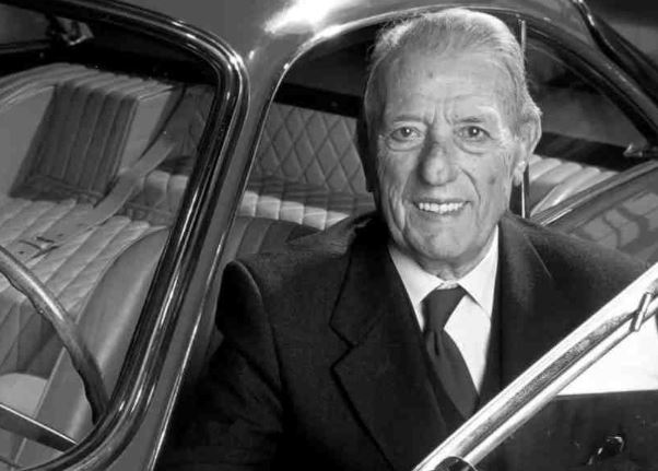 Portrait noir et blanc de Sergio Scaglietti assis à bord d’une Ferrari, figure majeure du carrossage italien.