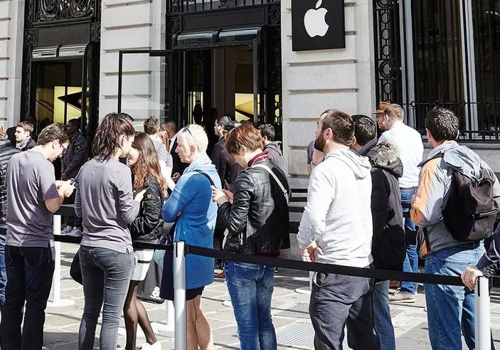 Personnes faisant la queue devant un magasin Apple en regardant leur smartphone