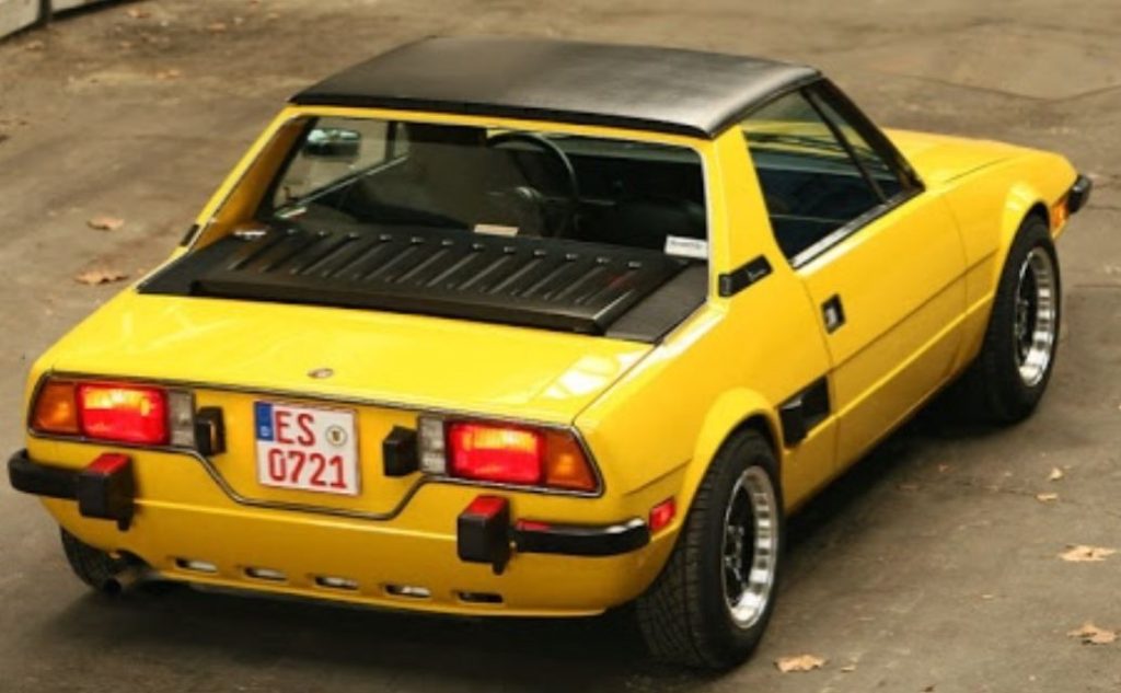 Fiat X1/9 jaune vue arrière avec capot moteur noir et pare-chocs d’origine