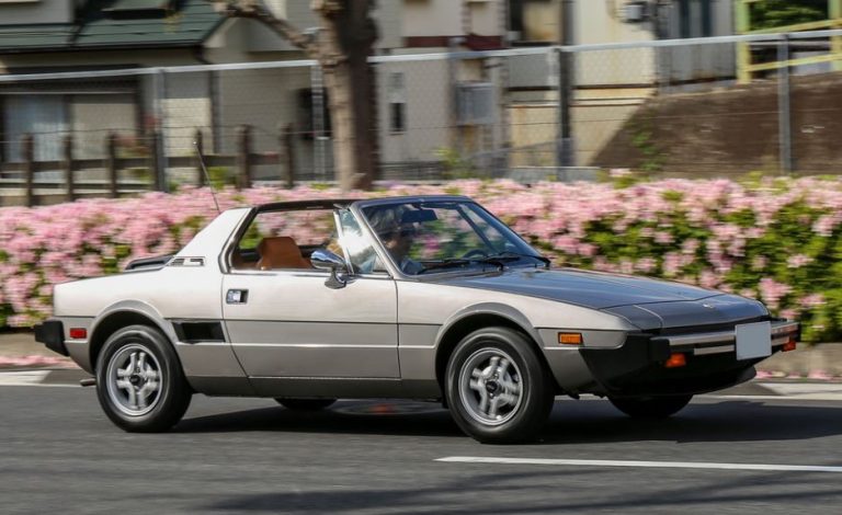 Fiat X1/9 grise en mouvement, profil typique moteur central et toit targa