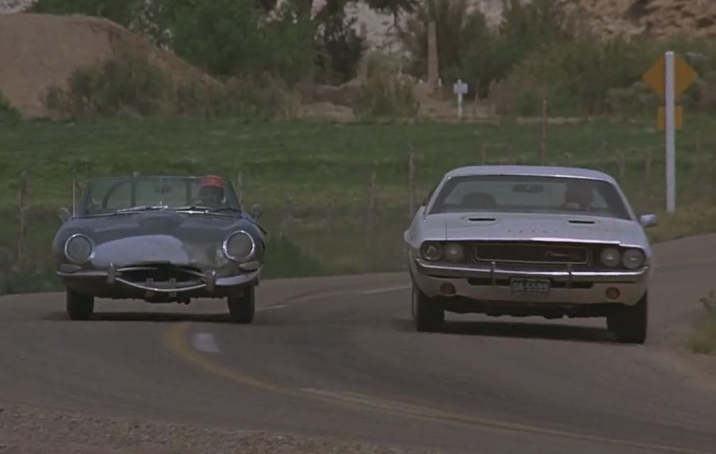 Dodge Challenger roulant aux côtés d’une Jaguar Type E dans Point Limit Zero