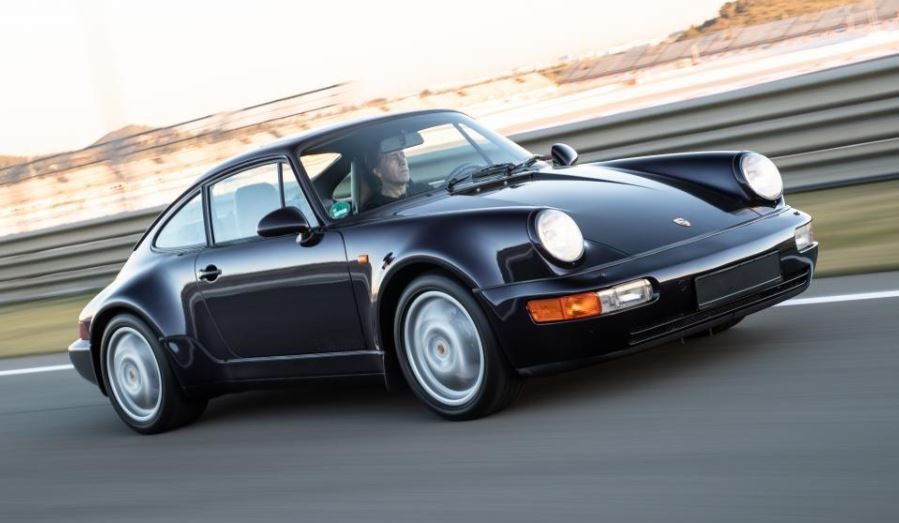 Porsche 911 964 Carrera 4 noire en mouvement sur route, coupé sportif emblématique des années 90