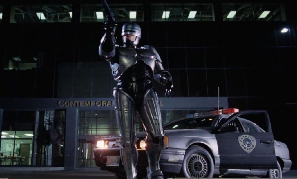 Voiture de police futuriste derrière Robocop dans une scène du film éponyme