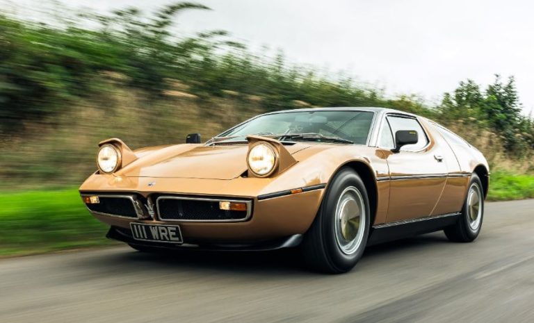Maserati Bora beige roulant sur route avec phares escamotables ouverts
