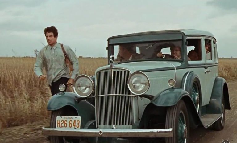 Clyde à côté d’une Ford V8 dans un champ aux États-Unis années 1930