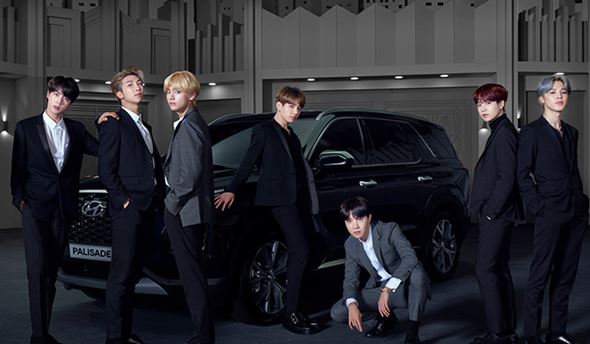 Membres de BTS posant devant un Hyundai Palisade noir dans un décor studio