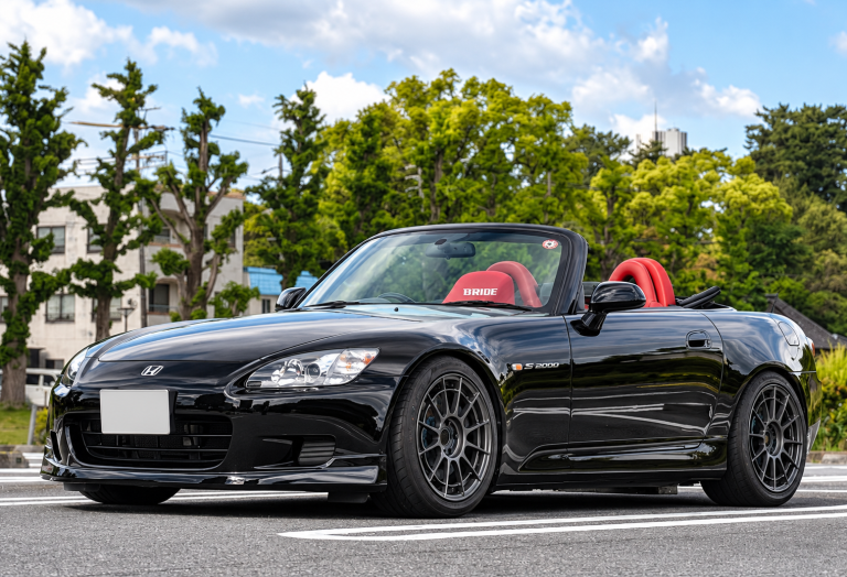 Honda S2000 noire décapotée vue de trois quarts avant, avec jantes sport et sièges rouges.