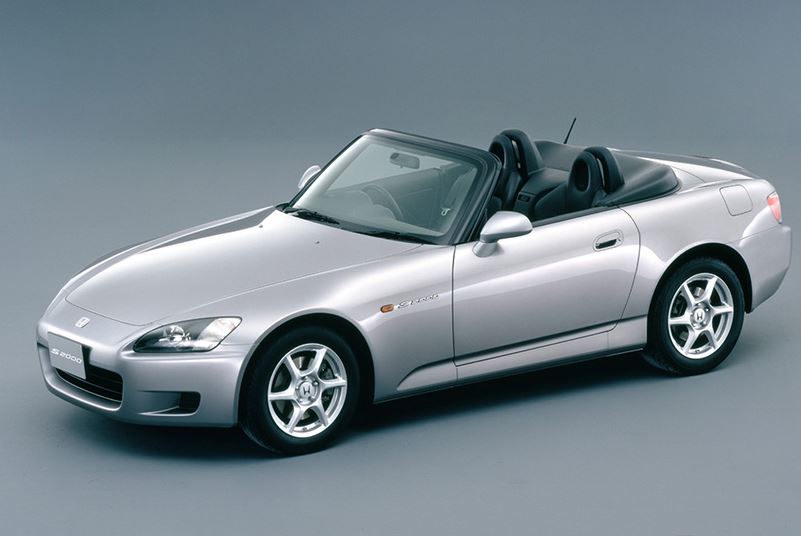 Honda S2000 grise décapotée photographiée de trois quarts avant sur fond neutre.
