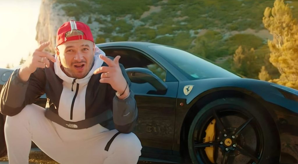 Jul devant une Ferrari noire dans le sud de la France