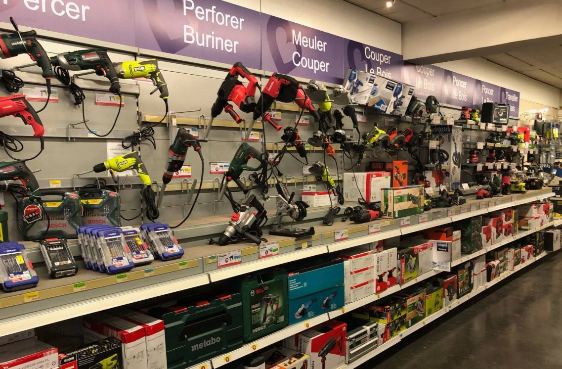 Rayon de magasin de bricolage présentant des outils électroportatifs de différentes gammes, illustrant le choix entre prix d'achat, qualité et durabilité des équipements.
