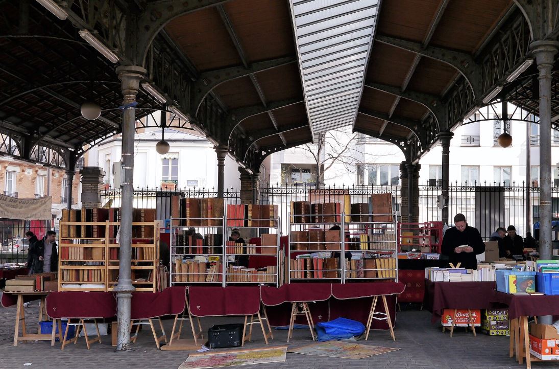 Marché aux livres d'occasion sous une halle couverte illustrant l'économie de la seconde main et la réutilisation des objets.