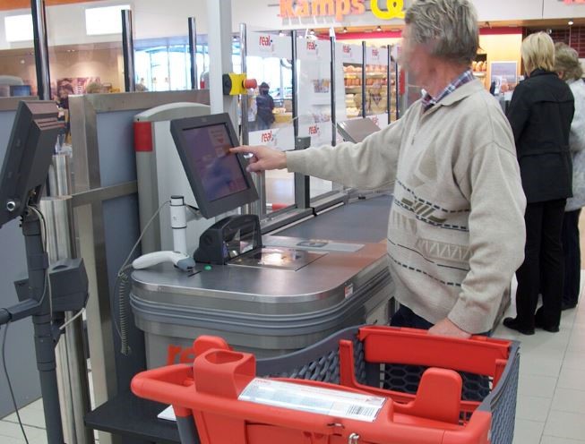 Client utilisant une caisse automatique dans un supermarché, illustrant l'automatisation croissante des services de paiement dans le commerce.