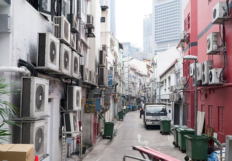 Rue urbaine bordée de nombreuses unités extérieures de climatisation, illustrant le rejet de chaleur dans l'espace public lors des épisodes de canicule.