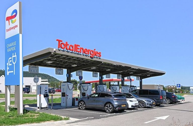 Station de recharge rapide sur une aire d'autoroute avec plusieurs voitures électriques en cours de recharge pendant les vacances d'été.