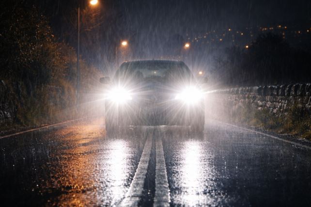 Phares modernes éblouissants d'une voiture circulant de nuit sous la pluie.