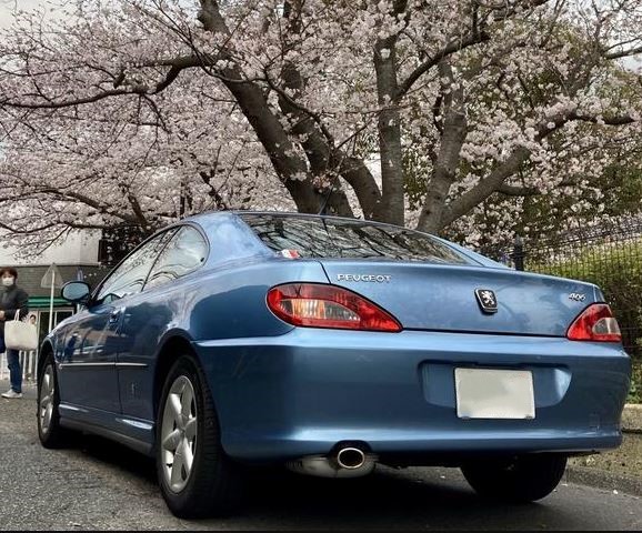 Peugeot 406 Coupé vue de trois-quarts arrière sous des arbres en fleurs.
