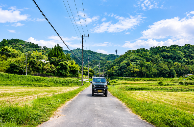 Voiture circulant sur une petite route de campagne au milieu des champs, où l’automobile reste souvent indispensable.