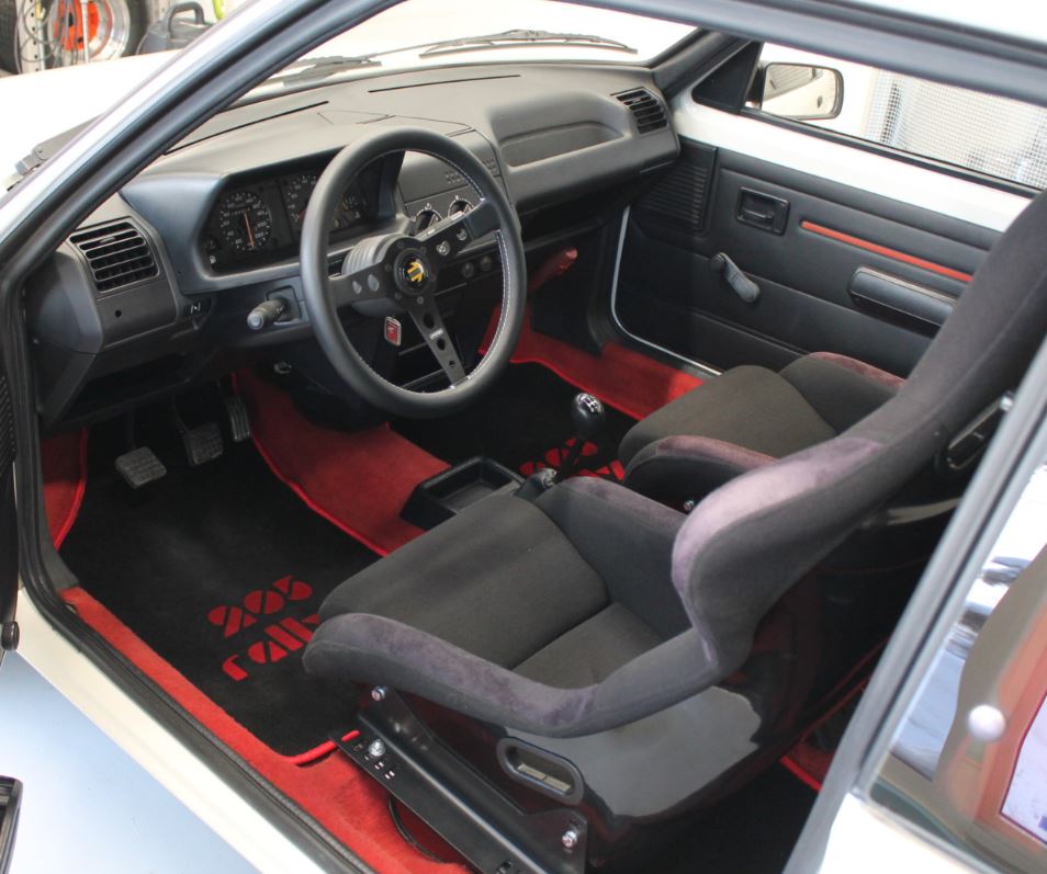 Habitacle d’une Peugeot 205 Rallye avec sièges baquets, volant sport et moquette rouge