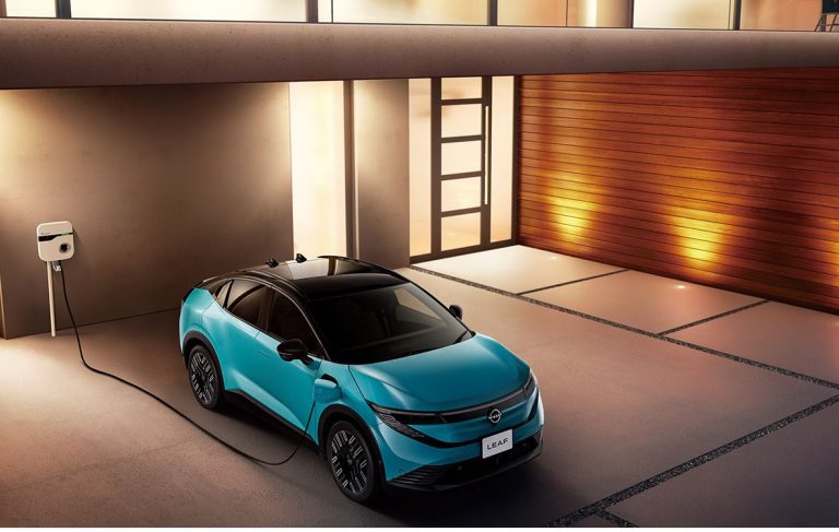 Nissan Leaf électrique bleu turquoise branchée à une borne de recharge domestique devant une maison moderne, illustrant la recharge à domicile pendant les heures creuses.